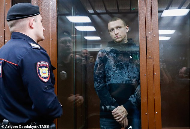 Mamayev stands behind a glass door during his hearing and is guarded by security officials