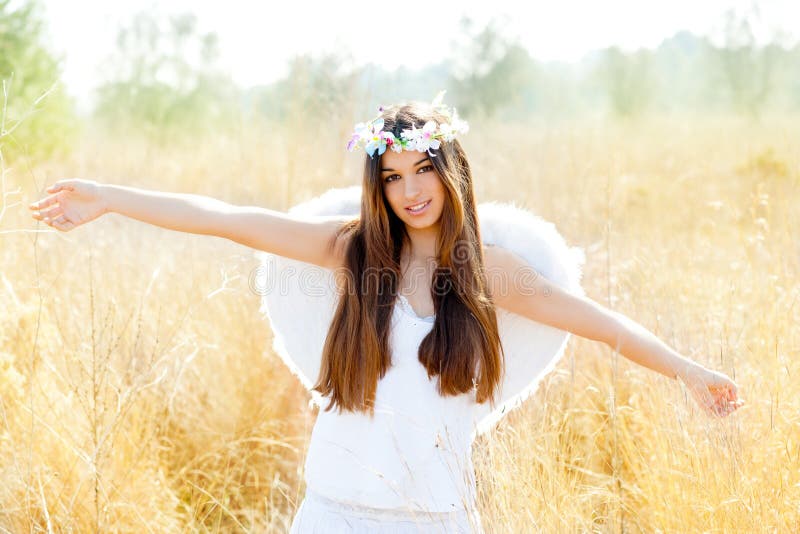 Angel girl in golden field with white wings. Angel etchnic woman in golden field with feather white wings and flowers crown royalty free stock image