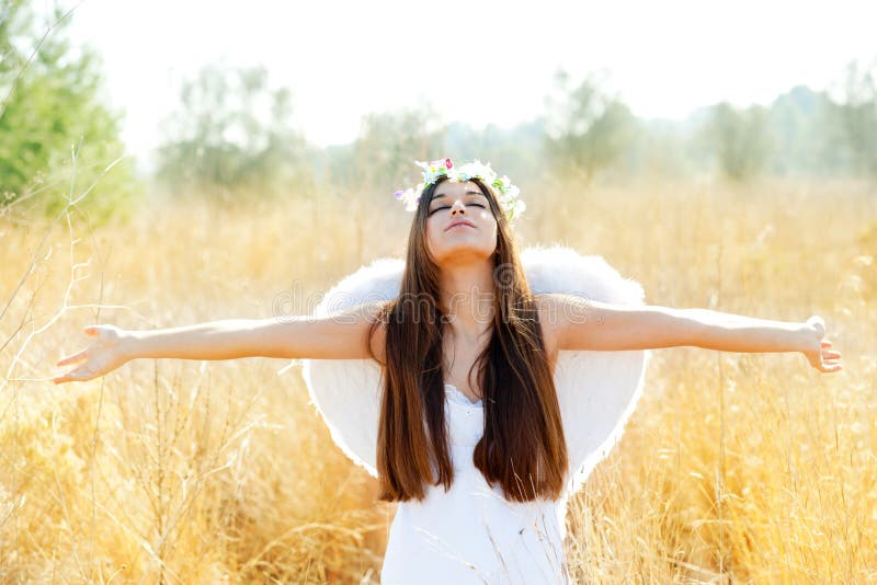 Angel girl in golden field with white wings. Angel etchnic woman in golden field with feather white wings and flowers crown royalty free stock photography
