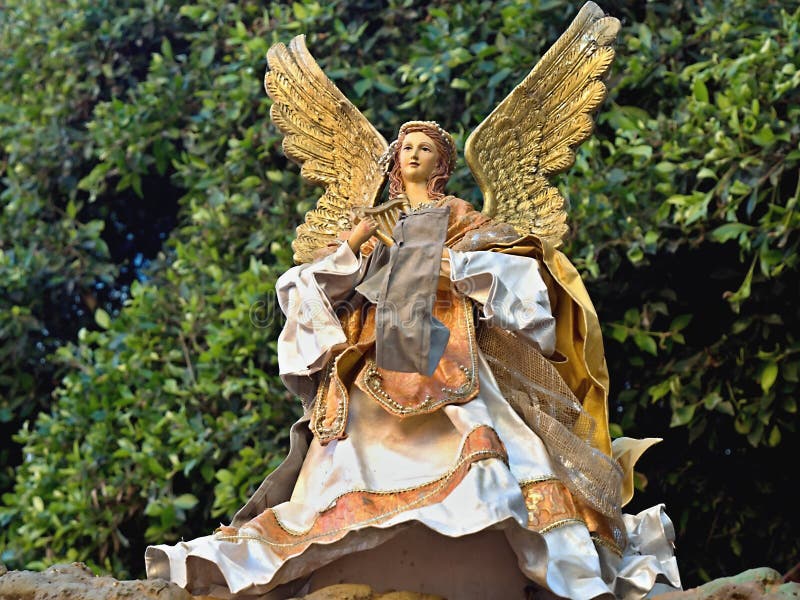 Big Christmas angel with golden wings and lush robe in gold and beige. He stands in front of an evergreen bush.The angel has a harp in her hand is female with stock photo