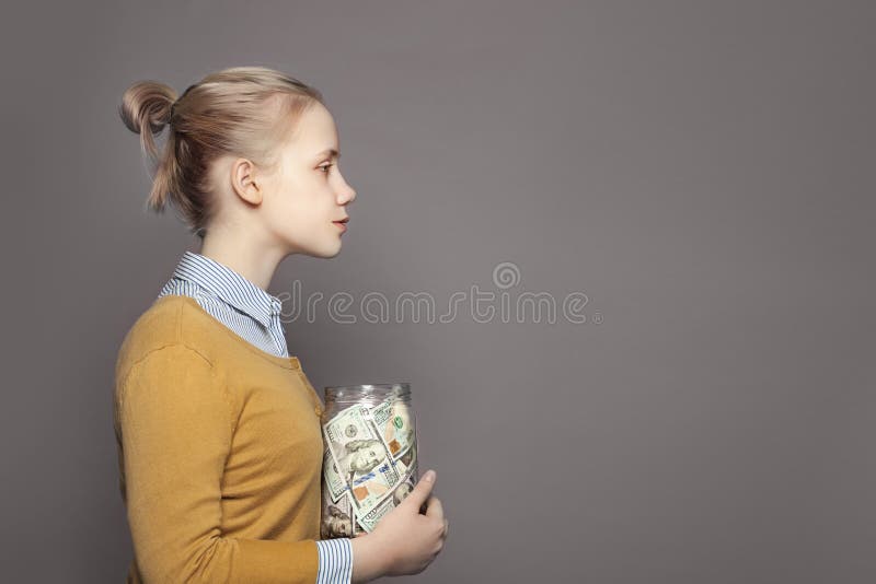 Cute young girl teenager saving money in glass jar. Education fees and saving money concept.  royalty free stock image