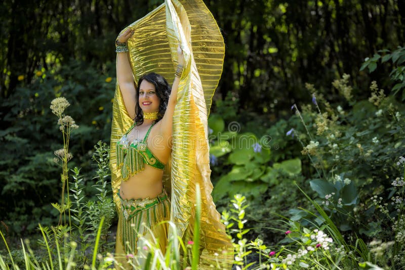 Dancer with golden Isis wings. Middle Eastern Belly Dancer with Golden Isis Wings poses in a green garden royalty free stock images