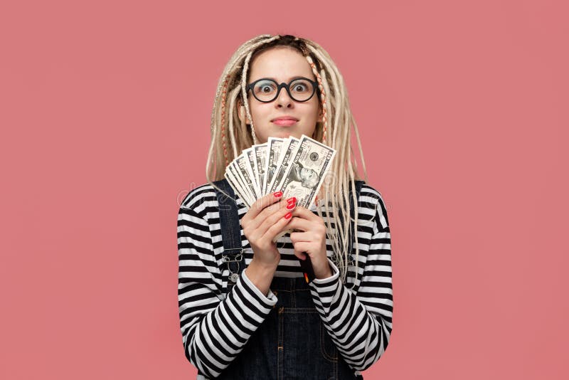 Excited teenager with dreadlocks in a striped shirt and jeans jumpsuit holding lots of cash. Being rich stock images