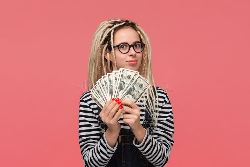 Excited teenager with dreadlocks in a striped shirt and jeans jumpsuit holding lots of cash. Being rich stock images