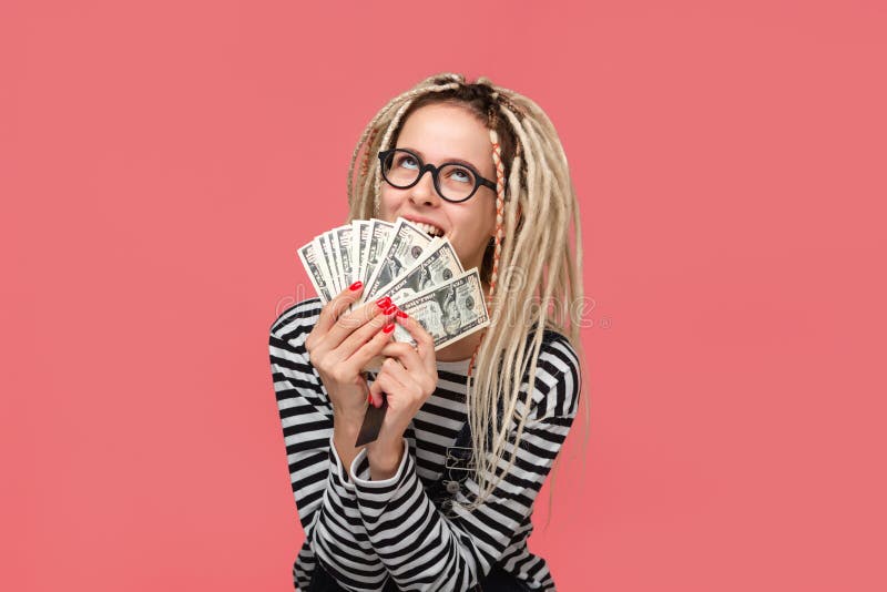 Excited teenager with dreadlocks in a striped shirt and jeans jumpsuit holding lots of cash. Being rich royalty free stock image