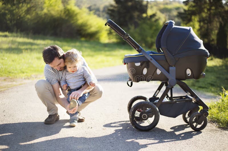 Father with little son and baby daughter in stroller. Sunny park. Young father outdoors in sunny summer park with cute little son and baby daughter in stroller stock photos