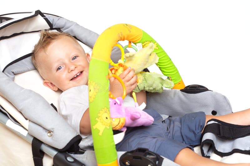 Happy baby in stroller. One year old baby boy is sitting in a stroller, smiling and playing with toys. All toys visible on the photo are officially property stock photography