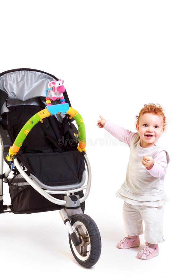 Happy baby and stroller. One year old red haired baby girl with baby stroller. Studio Shot. All toys visible on the photo are officially property released royalty free stock images