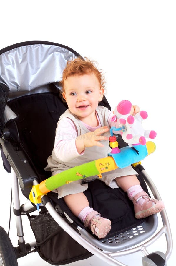 Happy baby in stroller. One year old red haired baby girl with baby stroller. Studio Shot. All toys visible on the photo are officially property released stock images
