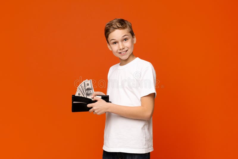 Happy little boy holding wallet with lots of dollars. Rich teenager. Happy little boy holding wallet with lots of dollars, orange studio background royalty free stock image