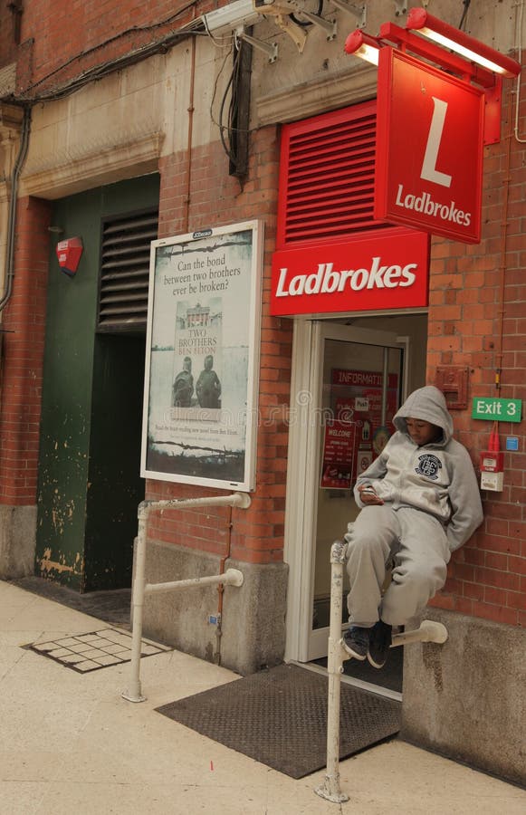 Ladbrokes betting shop. Hooded teenager sitting in front of Ladbrokes betting shop in Victoria station, London, UK stock photo