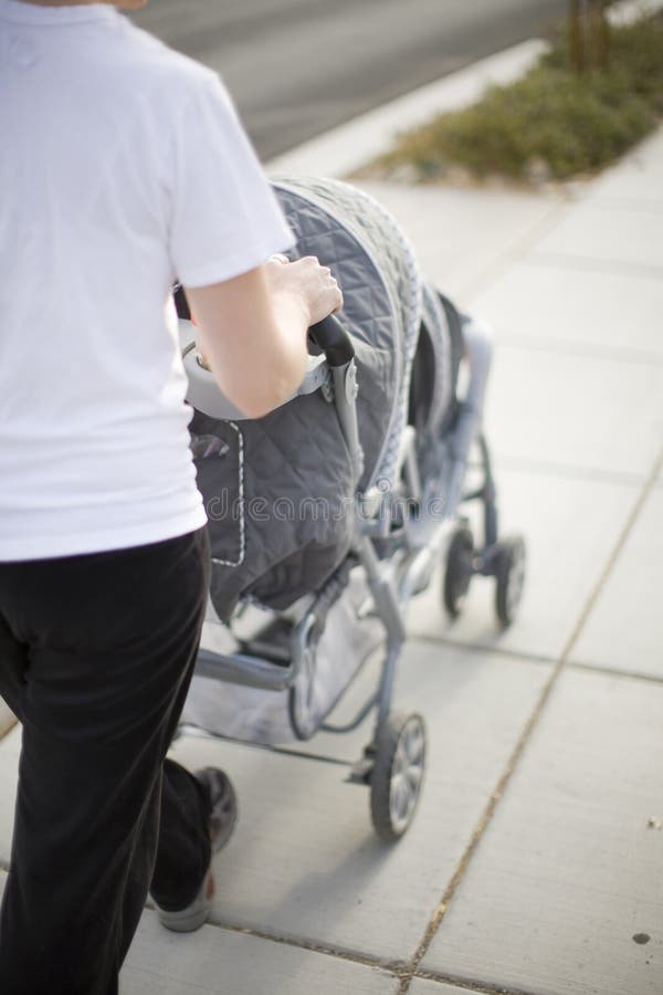 Mother and baby stroller. A mother wearing a white t-shirt is walking her babies on the sidewalk outside in a baby stroller stock images