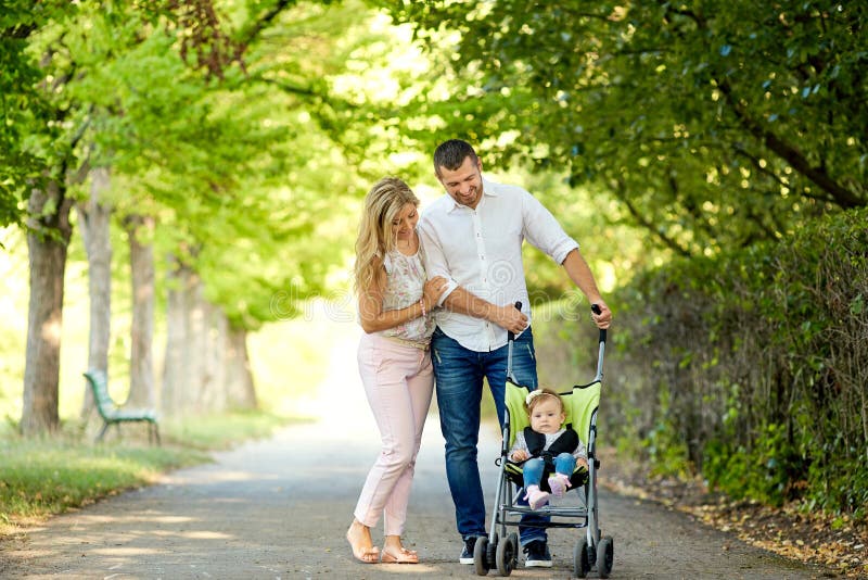 Mother, father and baby in a stroller walking in the park. Mother, father and baby in a stroller walk along the alley in the park royalty free stock images