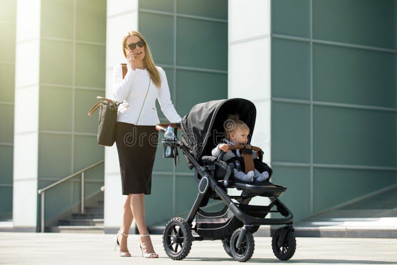 Woman talking on the phone and pushing baby stroller. Business women talking on the phone and pushing baby stroller royalty free stock photo